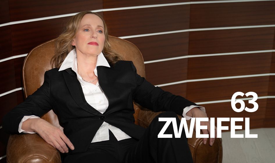 Frau im schwarzen Anzug sitzt souverän in einem Ledersessel vor dunkler Holzvertäfelung, daneben der Schriftzug „63 Zweifel“ – Blogartikel über Gene Key 63, Zweifel und Positionierung für vielbegabte Solopreneurinnen.